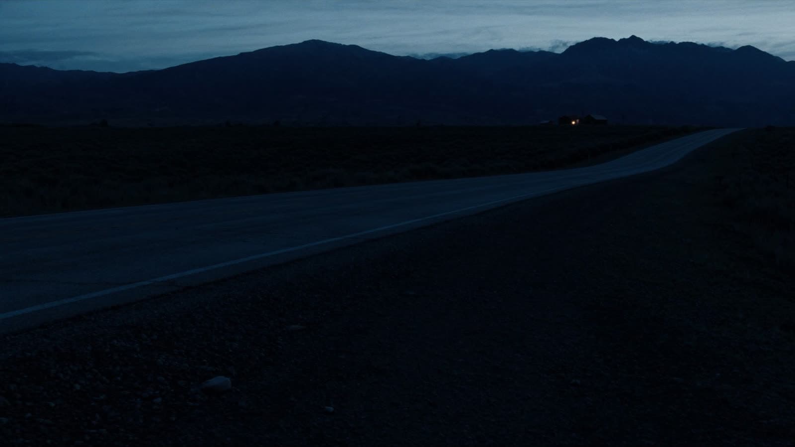 Dusk highway across open Montana ground with one ranch light in the distance