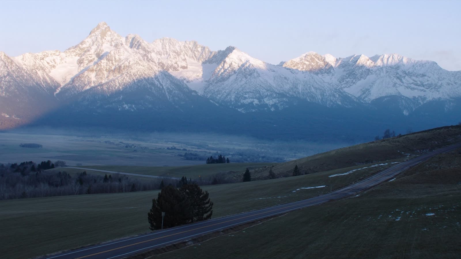 Winding rural Montana road toward a snow-covered mountain range